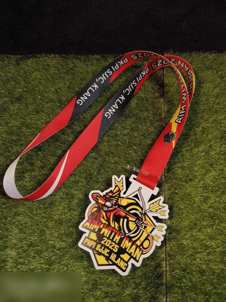 Medal 'AIM WITH IMAN 2025' PKPI SJJC Klang — kejohanan memanah. Bentuk custom dengan pemanah dan anak panah bergaya. Warna kuning, merah dan hitam. Lanyard panjang merah-hitam-putih bercetak penuh 'AI