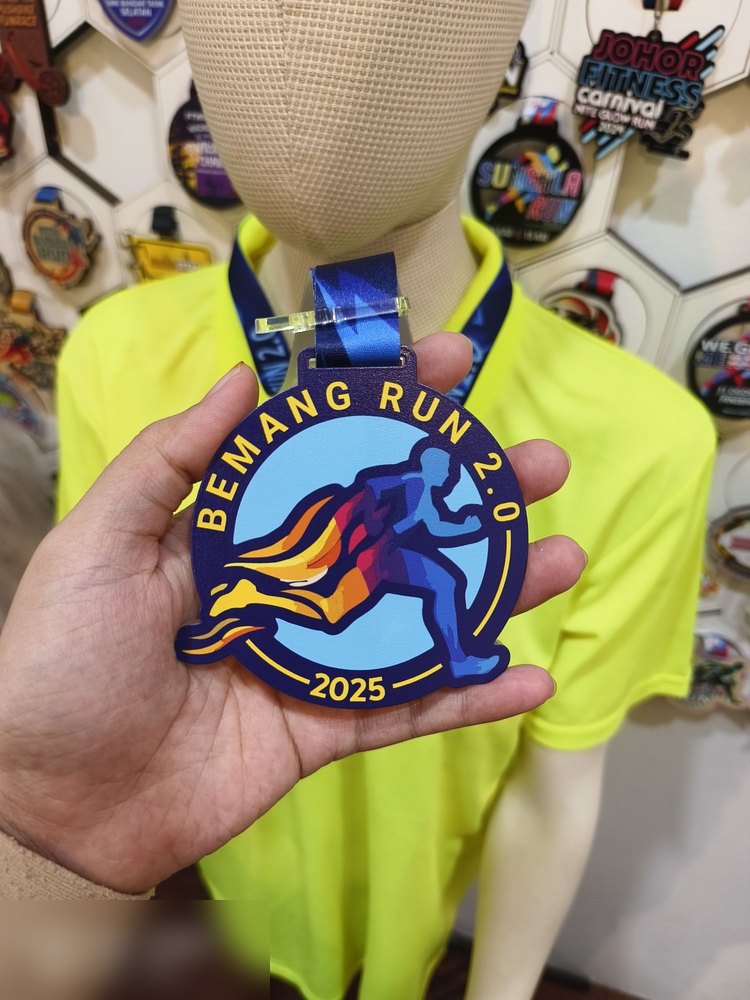 Medal Bemang Run 2.0 2025. Bentuk bulat biru gelap dengan pelari dan kesan api oren-kuning di belakang. Teks 'BEMANG RUN 2.0' melengkung dan '2025'. Reben biru berkilat. Digantung pada mannequin di ga