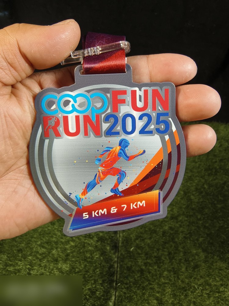Medal Coop Fun Run 2025 untuk kategori 5KM dan 7KM. Bentuk custom bulat dengan bahagian atas bertingkat. Latar perak brushed metal, pelari dalam gradasi biru-oren, teks 'COOP FUN RUN 2025' dan pita '5