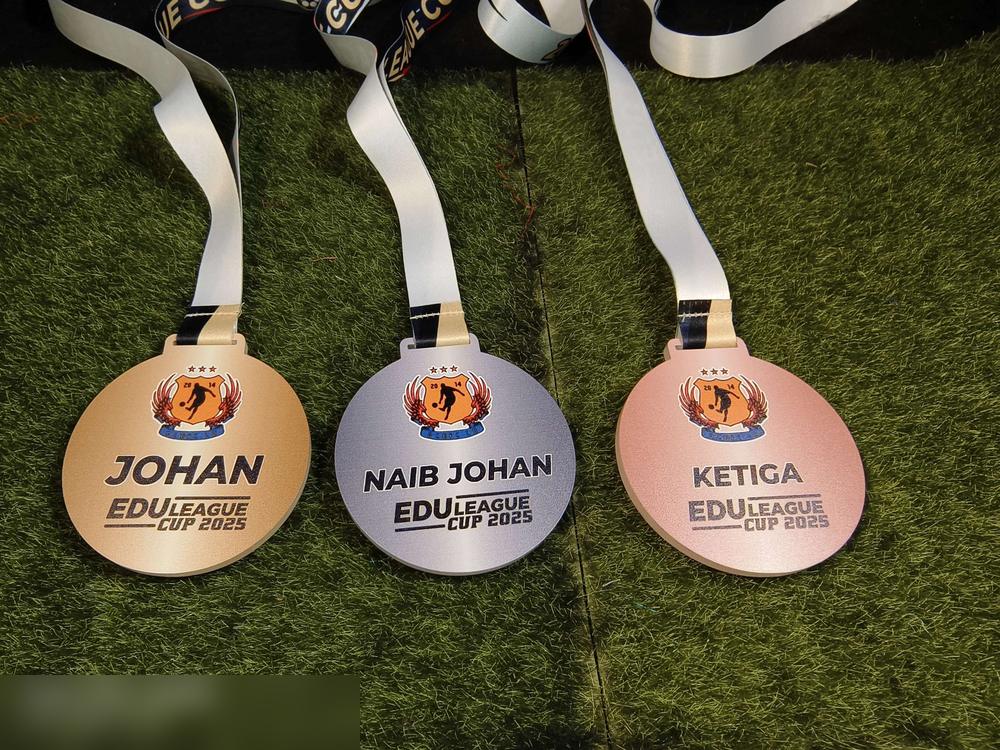 TIGA medal Edu League Cup 2025 bersebelahan menunjukkan PERBEZAAN WARNA mengikut kedudukan: EMAS untuk 'JOHAN', PERAK untuk 'NAIB JOHAN', dan GANGSA/tembaga untuk 'KETIGA'. Semua guna design dan logo 