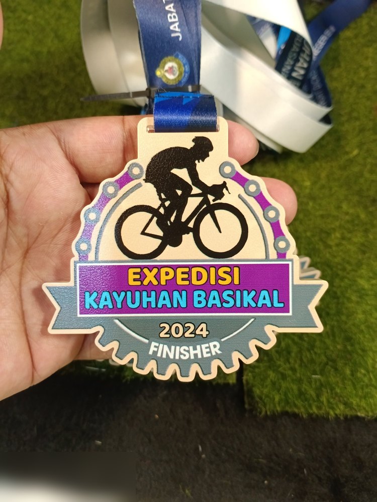 Medal Expedisi Kayuhan Basikal 2024 Finisher. Bentuk custom dgn bingkai RANTAI BASIKAL dan gear di bawah, latar krim dgn silhouette pelumba hitam, pita ungu dan biru. Lanyard biru jabatan. Contoh bing