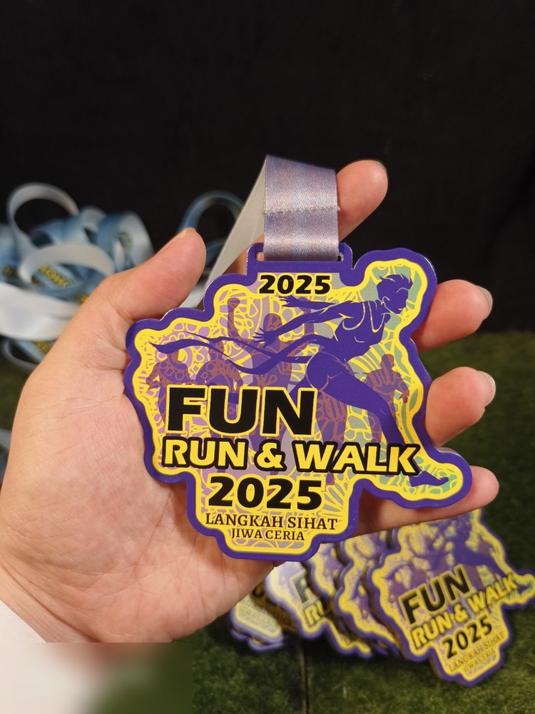 Medal Fun Run & Walk 2025 'Langkah Sihat Jiwa Ceria'. Bentuk custom dengan bingkai ungu tebal, corak batik/awan kuning di dalam dan silhouette pelari ungu. Reben ungu-perak. Warna ungu-kuning yang men