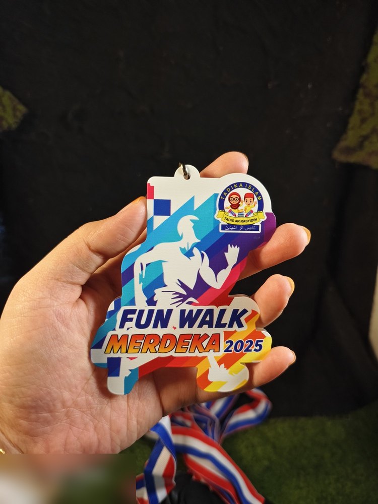 Medal Fun Walk Merdeka 2025 untuk Tadika Ar Rasyidin. Bentuk custom silhouette orang mengangkat tangan. Warna cerah biru, ungu, merah jambu, kuning dengan logo tadika. Lanyard jalur merah-putih-biru. 