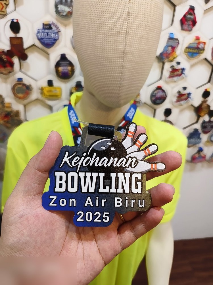Medal Kejohanan Bowling Zon Air Biru 2025. Bentuk custom dgn pin bowling dan bola di atas, gradasi BIRU ke EMAS. Teks 'Kejohanan' dlm tulisan sambung putih. Reben biru gelap.