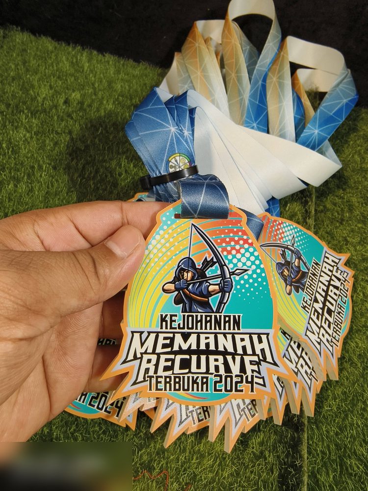 Medal Kejohanan Memanah Recurve Terbuka 2024. Bentuk custom bertepi tajam (spike), warna teal dan oren gradasi dgn corak halftone bertitik dan ilustrasi pemanah. Lanyard biru-putih bercorak geometri.