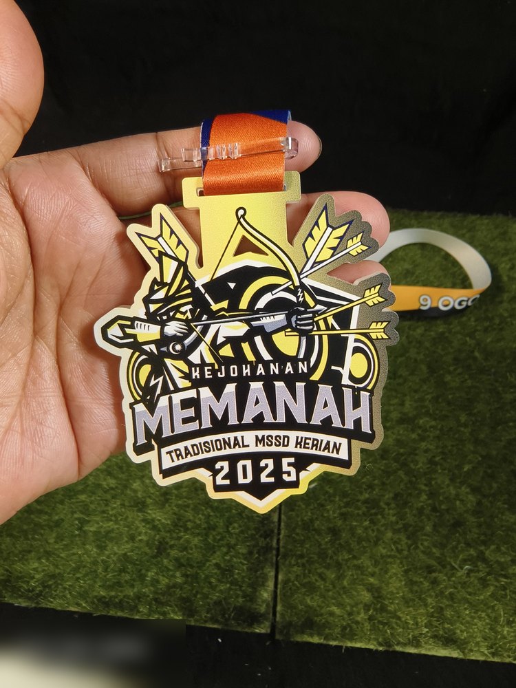 Medal memanah tradisional untuk MSSD Kerian 2025. Bentuk custom mengikut logo — pemanah menarik busur dengan anak panah dan sasaran bulatan di belakang. Warna kuning emas, hitam dan putih. Teks 'KEJOH