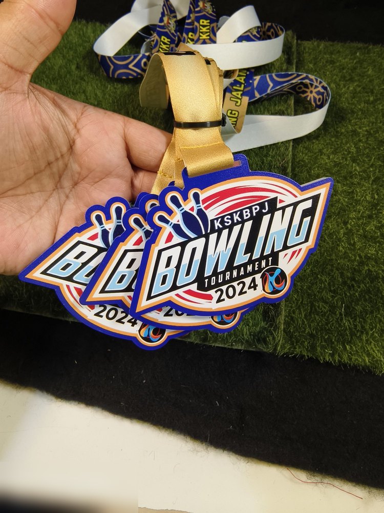 Medal KSKBPJ Bowling Tournament 2024. Bentuk custom dinamik dgn pin bowling di kiri, latar putih-merah dgn teks biru berbayang. Lanyard emas bercorak batik biru. Kombinasi lanyard batik + medal moden.