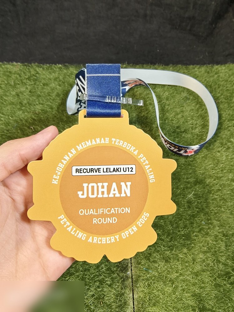 Bahagian BELAKANG medal Petala Open 2025 — warna emas dengan teks 'KEJOHANAN MEMANAH TERBUKA PETALING', kategori 'RECURVE LELAKI U12', pencapaian 'JOHAN' dan 'QUALIFICATION ROUND'. CONTOH TERBAIK untu
