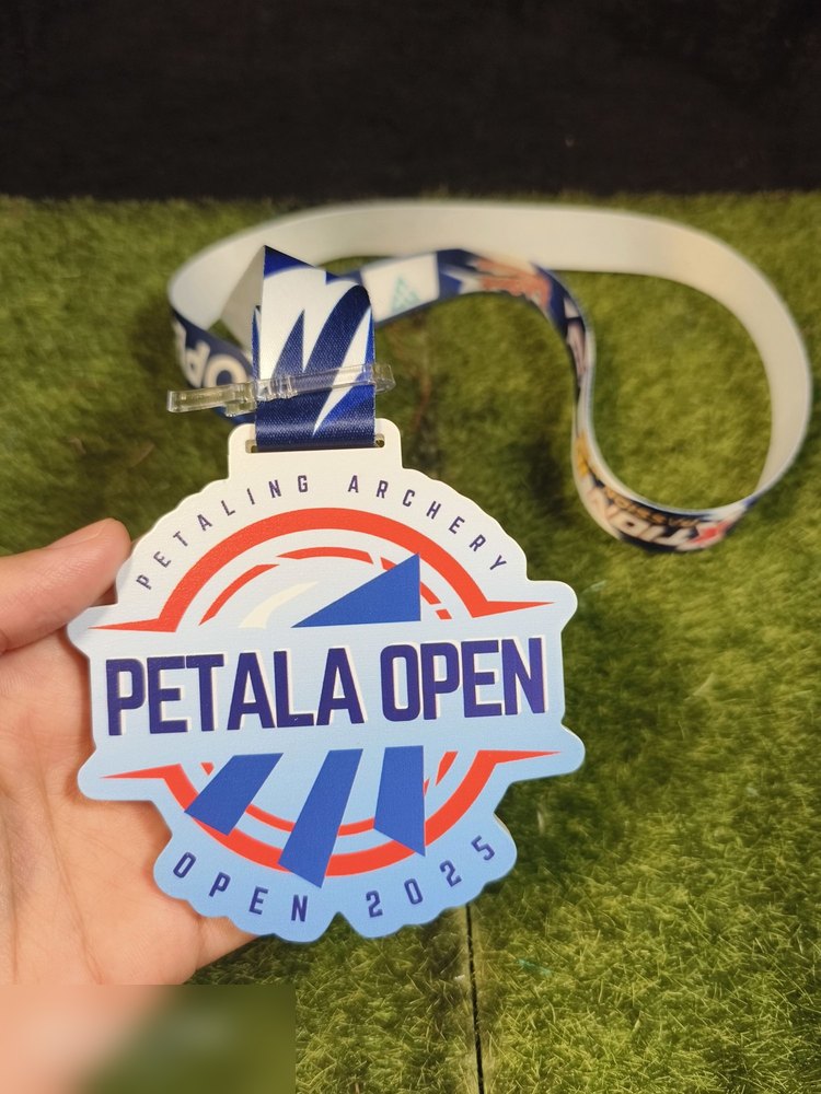 Medal Petala Open 2025 anjuran Petaling Archery. Bentuk custom bulat bergerigi di tepi. Warna putih, biru royal dan merah dengan corak anak panah bergaya. Teks 'PETALING ARCHERY - PETALA OPEN - OPEN 2