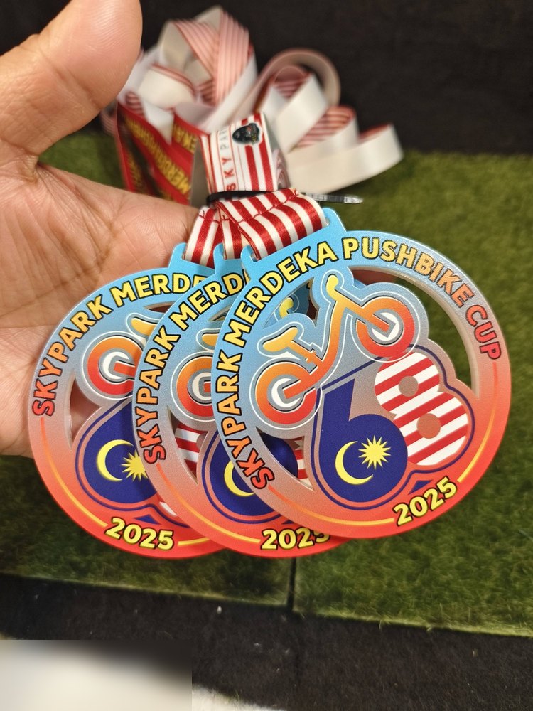 Medal Skypark Merdeka Pushbike Cup 2025 dalam kuantiti — beberapa keping bersusun menunjukkan potongan cut-out basikal dan lanyard jalur merah-putih. Bagus untuk tunjuk konsistensi kualiti untuk order