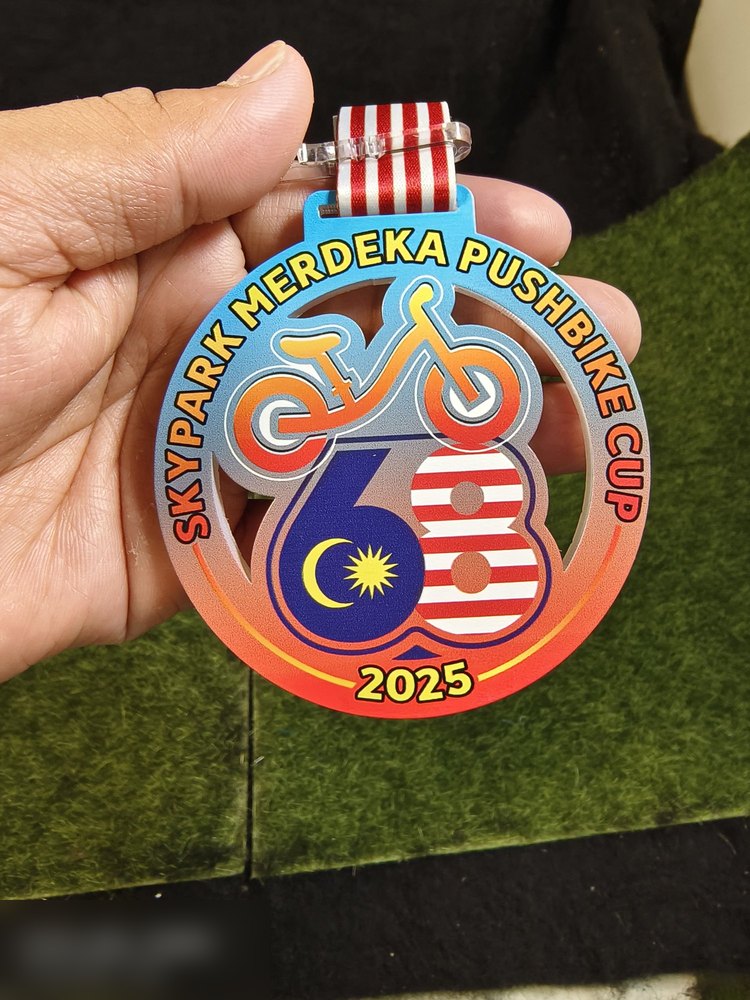 Medal Skypark Merdeka Pushbike Cup 2025 untuk perlumbaan pushbike kanak-kanak. Bentuk bulat dengan potongan berlubang (cut-out) di tengah bentuk basikal dan nombor 68 dengan Jalur Gemilang. Warna grad