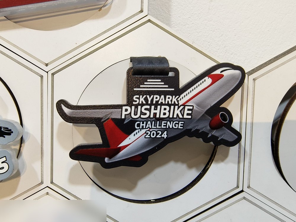 Medal Skypark Pushbike Challenge 2024 — dipotong mengikut bentuk KAPAL TERBANG (sesuai tema Skypark/lapangan terbang). Warna kelabu, merah dan hitam. Digantung dgn tab kulit. CONTOH TERBAIK untuk tunj