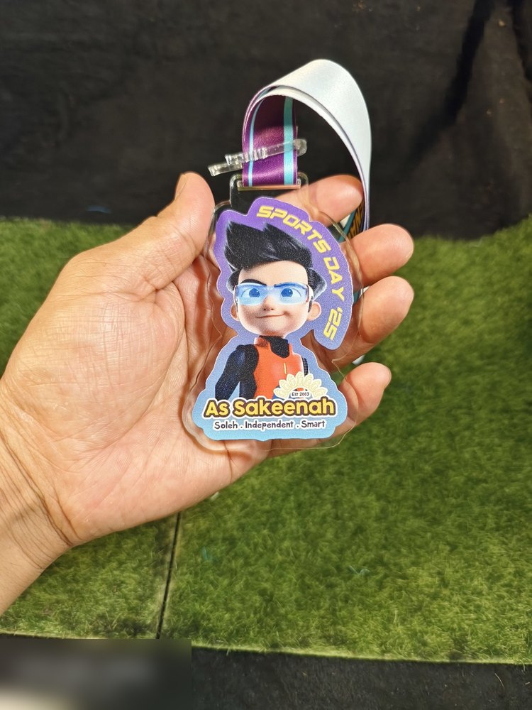 Medal Sports Day sekolah As Sakeenah 2025. Bentuk custom mengikut watak kartun budak lelaki berkaca mata memakai jersi oren. Warna ungu, oren dan putih. Teks 'SPORTS DAY 25', 'As Sakeenah', moto 'Sole