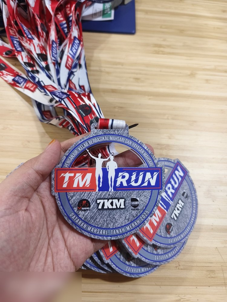 Medal TM RUN 7KM 2025 dalam kuantiti — beberapa keping bersusun dengan lanyard merah-putih-biru bercetak penuh. Bagus untuk tunjuk kepada customer rupa order pukal, bukan satu keping.