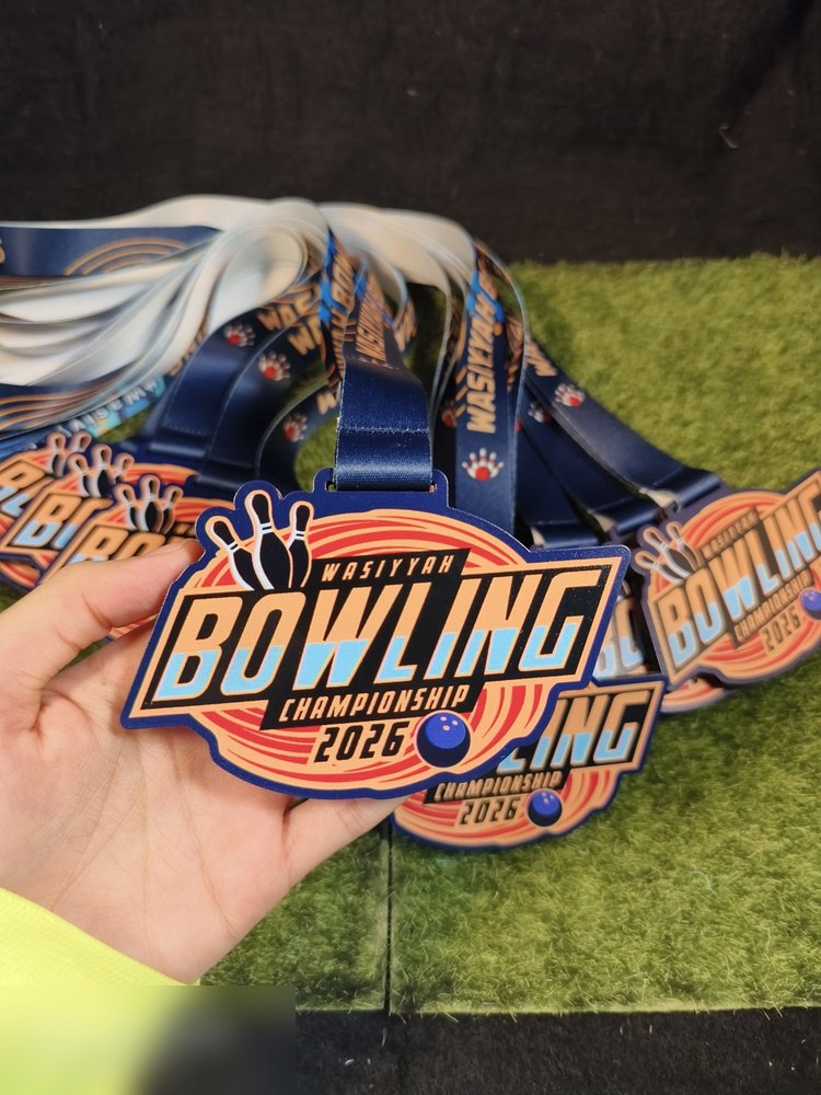 Medal Wasiyyah Bowling Championship 2026 dlm kuantiti — tunjuk warna navy, oren dan biru muda konsisten merentas banyak keping, dgn lanyard biru bercetak. Sudut berbeza daripada gambar sekeping.